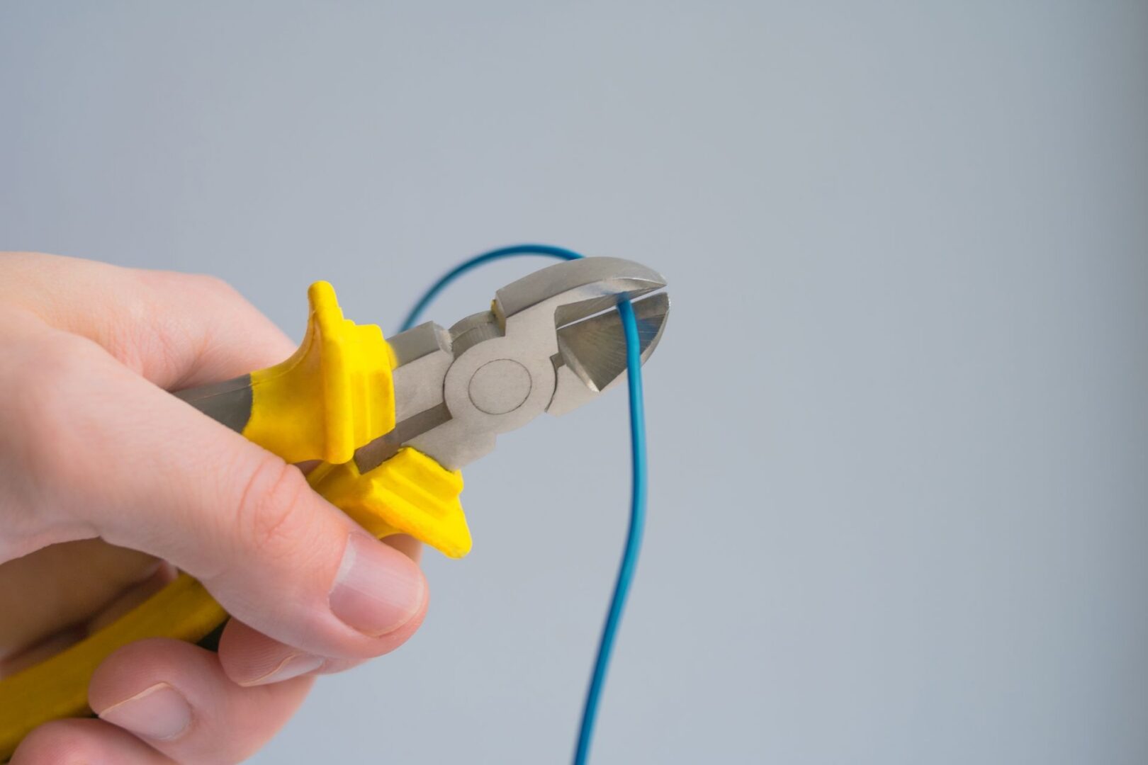 a person cutting a blue wire with a pair of pliers.